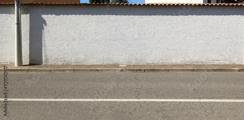 Long white stucco surrounding wall with rooftiles on top. Sidewalk and street in front. Background for copy space. photo