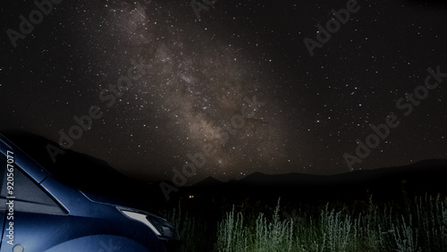 A starry night sky with the Milky Way visible above a car's silhouette and distant mountains