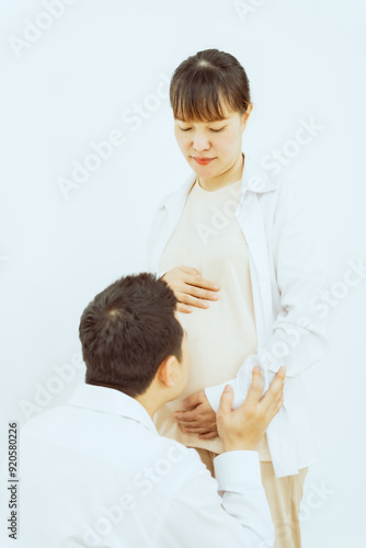 A middle-aged Asian couple, with the woman being pregnant, shares a loving embrace, smiling with happiness and anticipation for their soon-to-arrive baby, symbolizing family togetherness and joy.