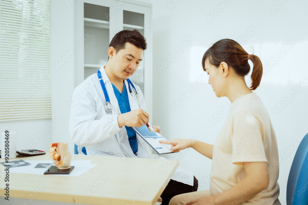 A male Asian pediatrician in a white lab coat sits at his desk, warmly greeting a middle-aged pregnant woman for a prenatal consultation, offering care and support in a clinical setting. A male Asian pediatrician in a white lab coat sits at his desk, warmly greeting a middle-aged pregnant woman for a prenatal consultation, offering care and support in a clinical setting.