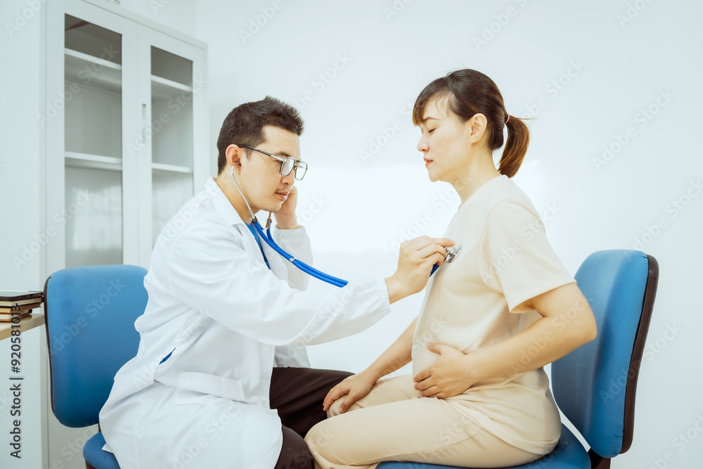 A male Asian pediatrician in a white lab coat sits at his desk, warmly greeting a middle-aged pregnant woman for a prenatal consultation, offering care and support in a clinical setting. A male Asian pediatrician in a white lab coat sits at his desk, warmly greeting a middle-aged pregnant woman for a prenatal consultation, offering care and support in a clinical setting.