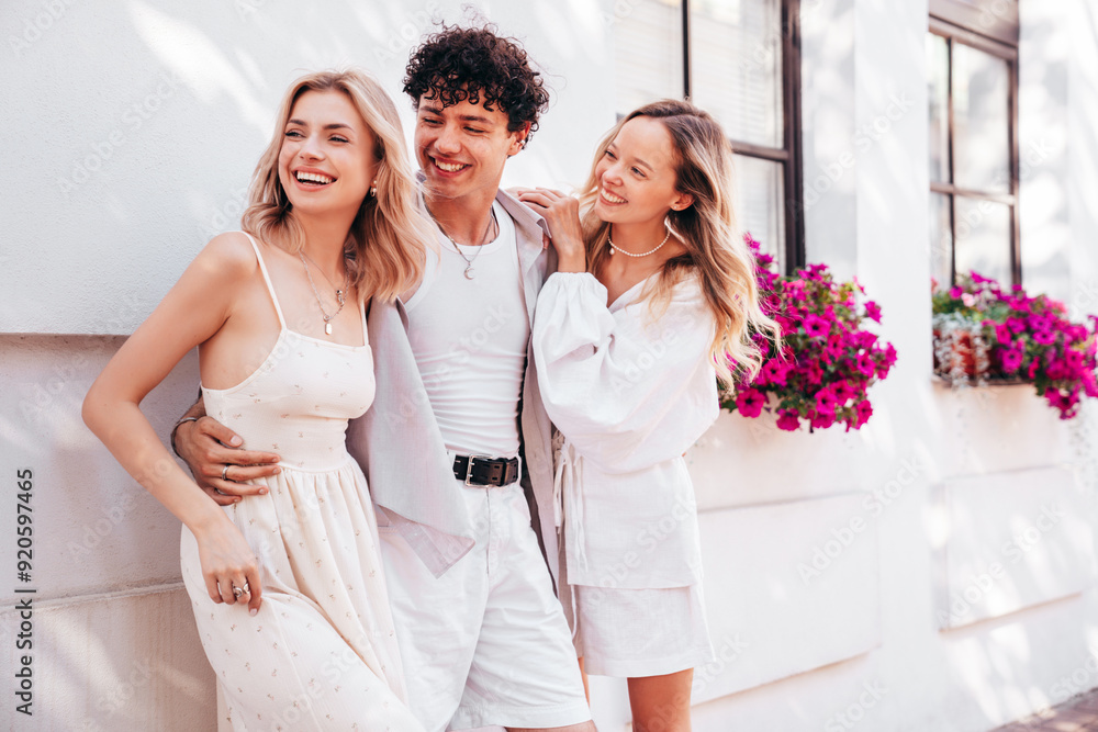 Young three stylish friends posing in the street. Fashion man and two cute female dressed in casual summer clothes. Smiling models having fun. Cheerful women and guy outdoors, in sunny day, near wall Young three stylish friends posing in the street. Fashion man and two cute female dressed in casual summer clothes. Smiling models having fun. Cheerful women and guy outdoors, in sunny day, near wall