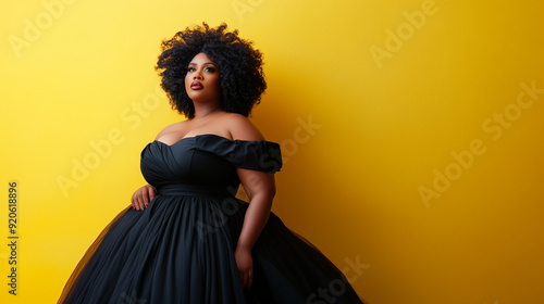 A full body photo of an African American woman with natural hair, plus size model wearing a black off the shoulder ball gown dress against a solid yellow background, with professio photo