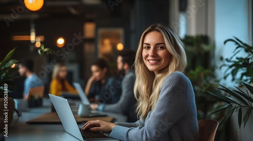 Businesswoman working on a laptop at her desk, with her team collaborating in the background