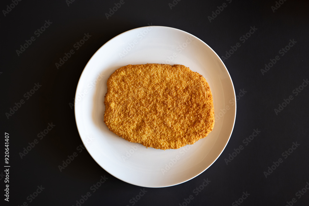 Raw, golden, bread crumb chicken schnitzel on a white plate. Top view, no people Raw, golden, bread crumb chicken schnitzel on a white plate. Top view, no people