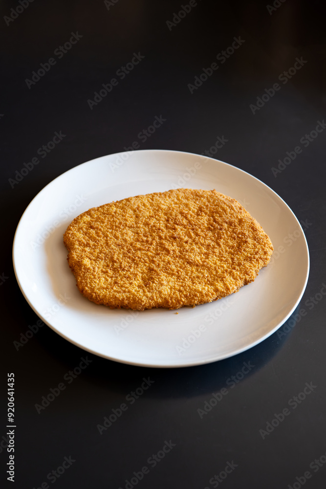 Raw, golden, bread crumb chicken schnitzel on a white plate. Top view, no people Raw, golden, bread crumb chicken schnitzel on a white plate. Top view, no people