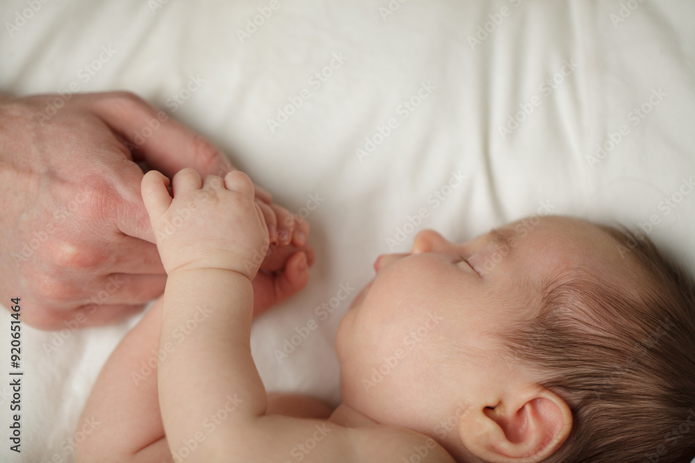 Adorable Newborn Baby Sleeping with father hand on White Bed Background with copy space Adorable Newborn Baby Sleeping with father hand on White Bed Background with copy space