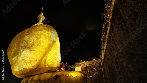 A large rock with a gold top is on a hill. People are gathered around it