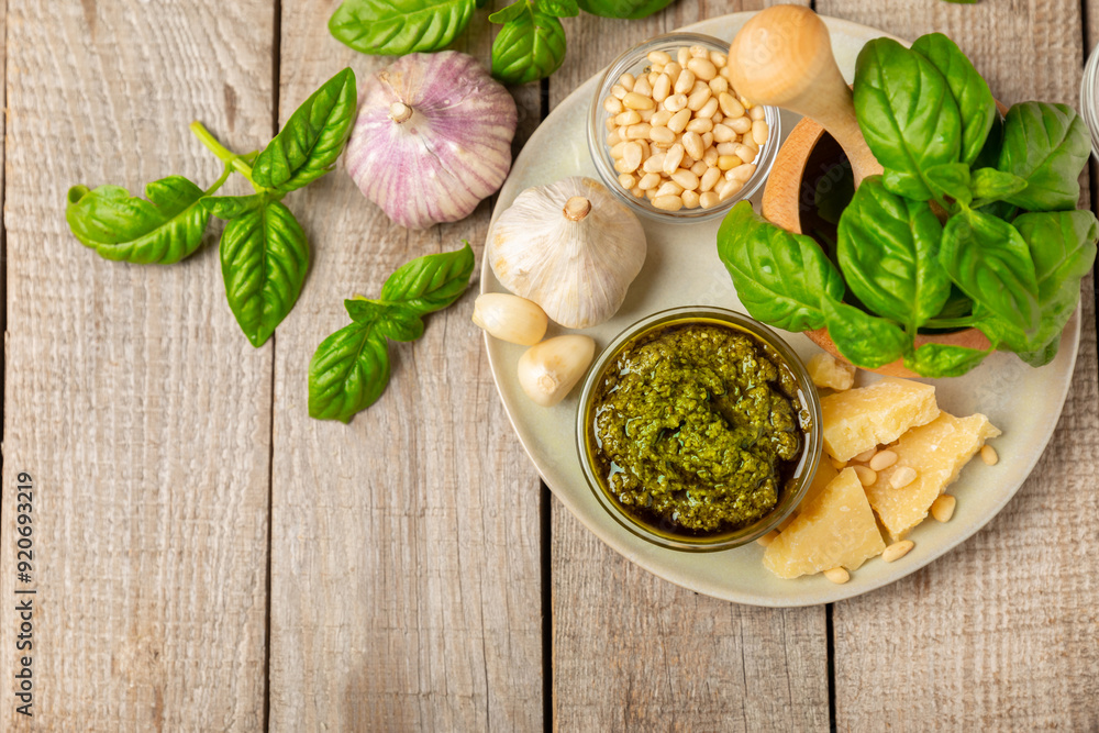 Pesto. Italian basil pesto sauce on a textured wooden background. Ingredient for pesto sauce: fresh basil, pine nuts, Parmesan cheese and olive oil. Space for text.Copy space. Pesto. Italian basil pesto sauce on a textured wooden background. Ingredient for pesto sauce: fresh basil, pine nuts, Parmesan cheese and olive oil. Space for text.Copy space.