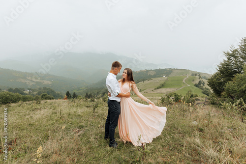 A couple is standing in a field, with the woman wearing a pink dress