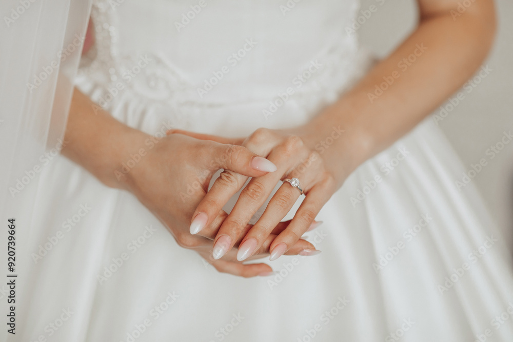 A woman is wearing a white dress and holding her hands together. She is wearing a diamond ring on her left hand A woman is wearing a white dress and holding her hands together. She is wearing a diamond ring on her left hand