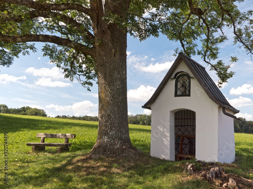 kleine Kapelle mit Sitzbank unter einem alten Baum photo