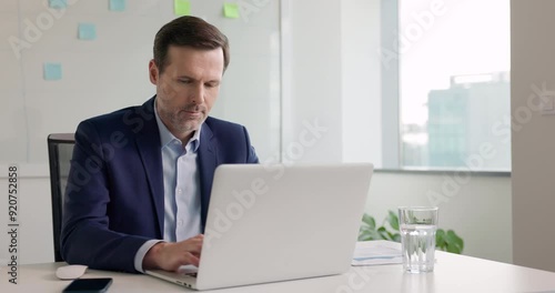 Businessman working on laptop sitting at desk in modern office