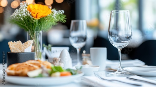 Fototapeta Naklejka Na Ścianę i Meble -  An upscale restaurant table set for breakfast or brunch with a fresh meal, including bread, vegetables, a small vase with flowers, and wine and water glasses on a white tablecloth.