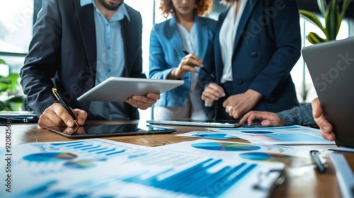 A group of business professionals collaborate over a table covered in charts and graphs.