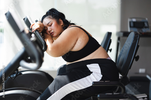 Tired fat asian woman on cycling. beautiful young chubby overweight woman wearing sporty fitness clothes doing exercise indoors at gym fitness sport club, body and health care