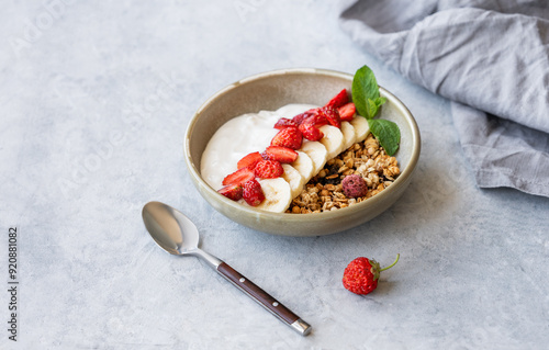 Natural greek yogurt with granola, strawberry and banana in a bowl on a light background with fresh berries, spoon and napkin. photo