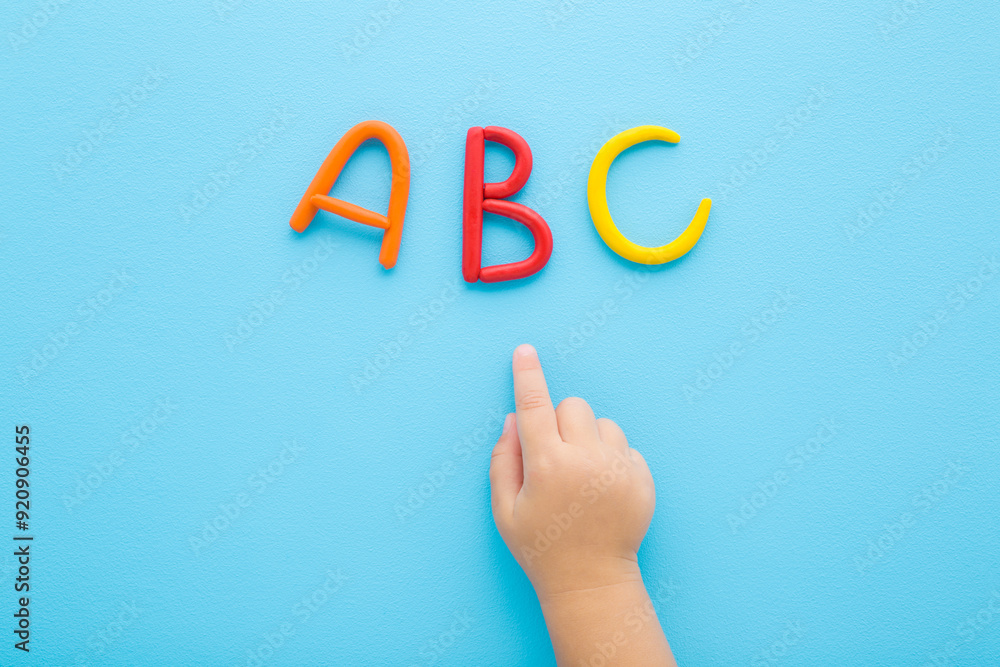Baby boy hand finger pointing to colorful 123 numbers created from modeling clay on light blue table background. Pastel color. Time to learning. Closeup. Top down view. Baby boy hand finger pointing to colorful 123 numbers created from modeling clay on light blue table background. Pastel color. Time to learning. Closeup. Top down view.