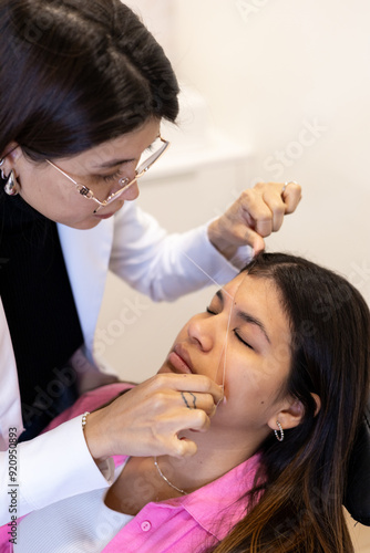 Beautician doing eyebrow threading design procedure. Young latin woman in a professional beauty salon for threading and brow shape correction 