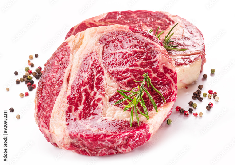 Obraz premium Raw beef steaks with herbs and spices ready for cooking on white background.