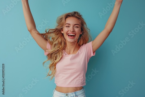 Joyful Blonde Woman Jumping in Air, Pink Shirt, White Jeans on Blue Background photo