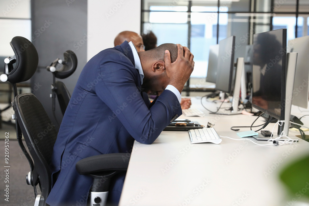 Businessman sitting with head in hands at desk in office Businessman sitting with head in hands at desk in office