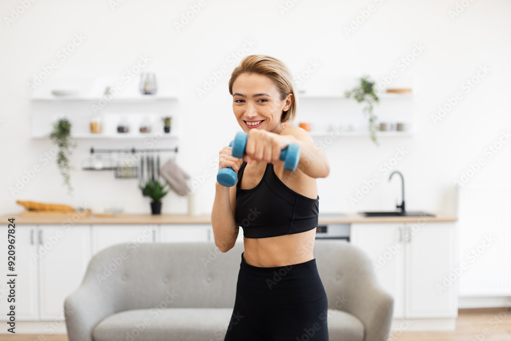 Woman in athletic wear working out with dumbbells in bright modern home interior, smiling while performing exercise routine, promoting fitness and healthy lifestyle Woman in athletic wear working out with dumbbells in bright modern home interior, smiling while performing exercise routine, promoting fitness and healthy lifestyle
