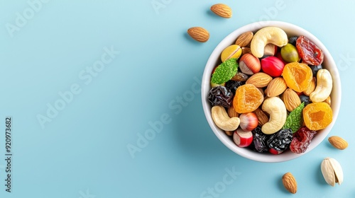 Top view of a bowl filled with a mix of dried fruits and various nuts on a blue background. Healthy snack option with colorful ingredients.