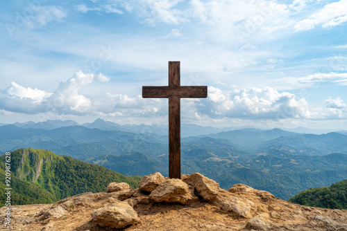 Wooden cross on a mountaintop with scenic mountain range and sky in the background, symbolizing faith and spirituality.