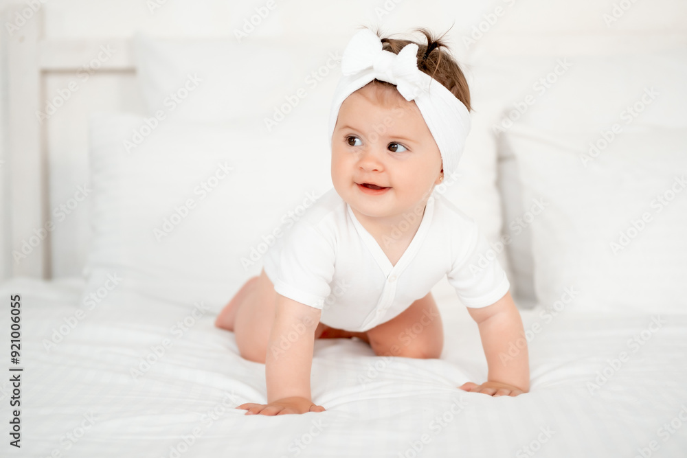 smiling little child or baby girl in a white bodysuit on the bed rejoices, healthy happy baby in the bedroom, space for text smiling little child or baby girl in a white bodysuit on the bed rejoices, healthy happy baby in the bedroom, space for text