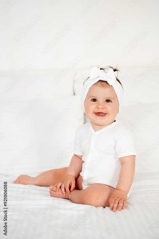 smiling little baby girl in a white bodysuit on the bed rejoices, healthy happy baby in the bedroom, space for text smiling little baby girl in a white bodysuit on the bed rejoices, healthy happy baby in the bedroom, space for text