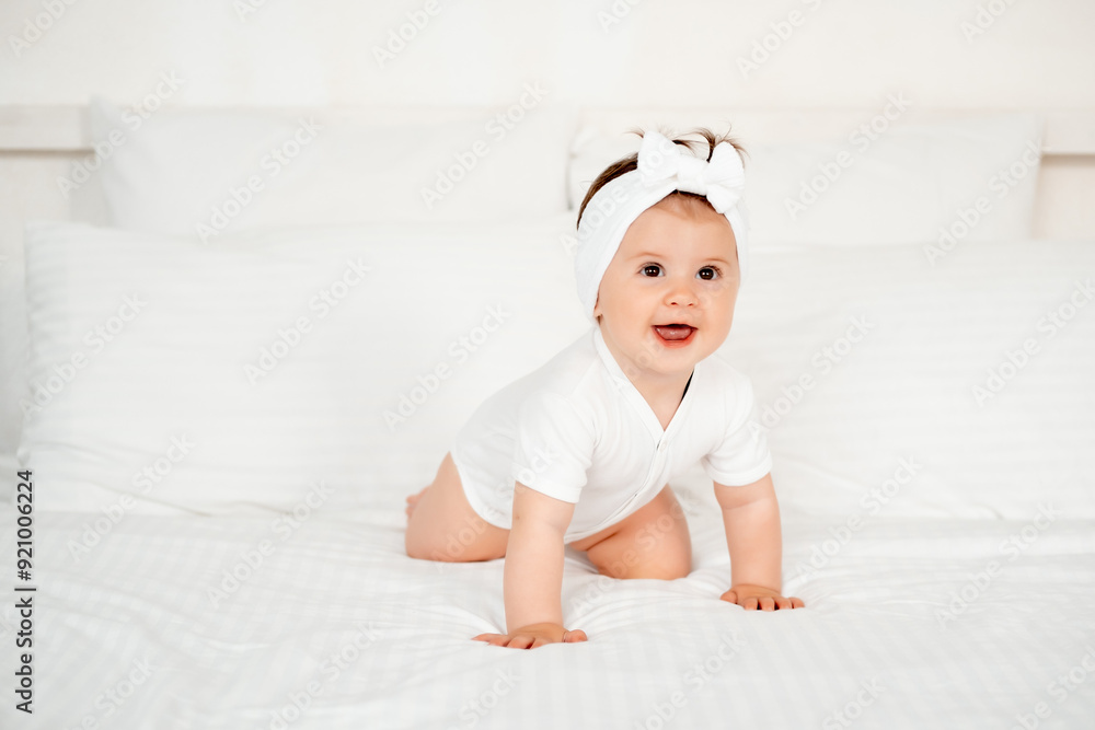 smiling little child or baby girl in a white bodysuit on the bed rejoices, healthy happy baby in the bedroom, space for text smiling little child or baby girl in a white bodysuit on the bed rejoices, healthy happy baby in the bedroom, space for text