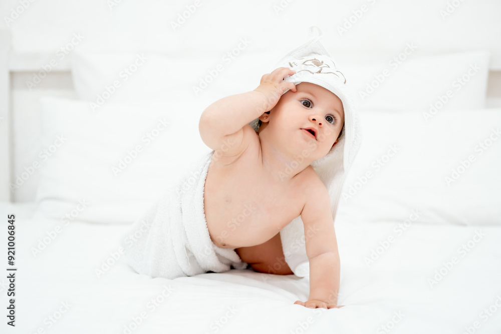 a baby in a towel on a white bed at home, a smiling child after bathing in a bright bedroom, a space for text a baby in a towel on a white bed at home, a smiling child after bathing in a bright bedroom, a space for text