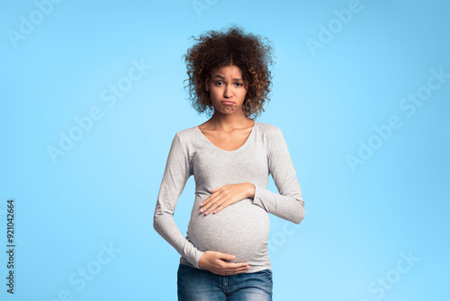 Hormones and mood changes. Sad expectant woman touching belly over grey studio background