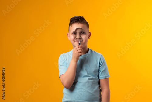 Child boy looking through magnifier over yellow background. Education and curiosity concept