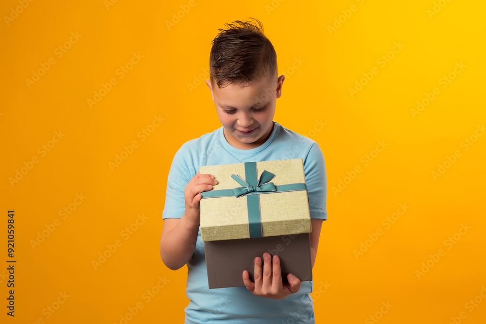 Child boy holding giftbox and looking inside the box over yellow background. Birthday and celebration concept Child boy holding giftbox and looking inside the box over yellow background. Birthday and celebration concept