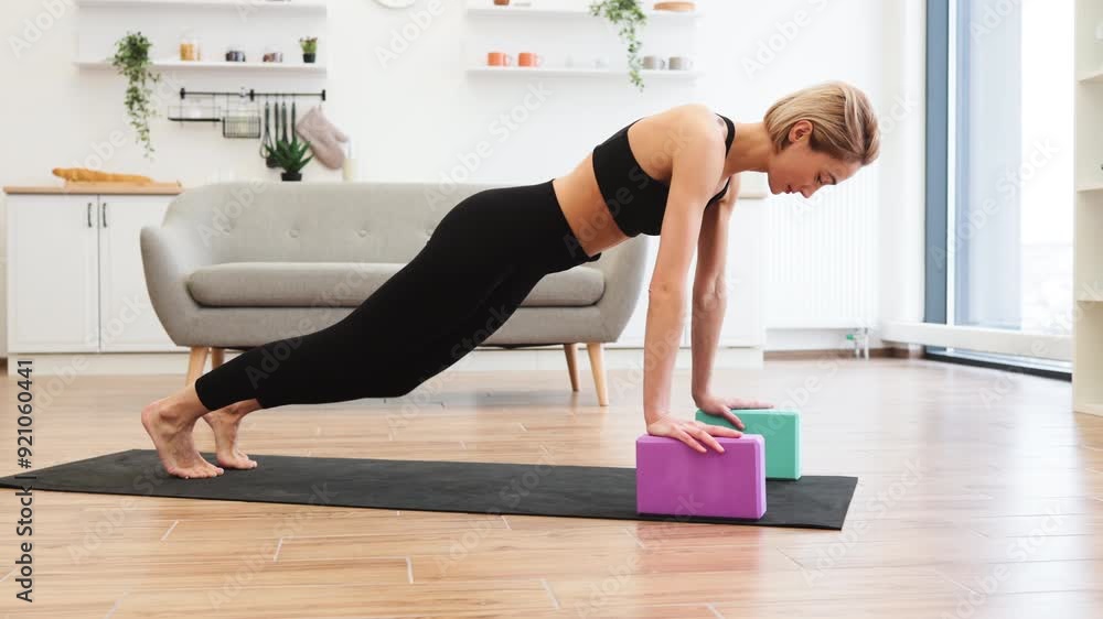Woman practicing yoga at home using yoga blocks in bright, modern living room. Wearing black sportswear performing plank pose on mat. Clean and stylish interior with wooden floor and natural light. Woman practicing yoga at home using yoga blocks in bright, modern living room. Wearing black sportswear performing plank pose on mat. Clean and stylish interior with wooden floor and natural light.