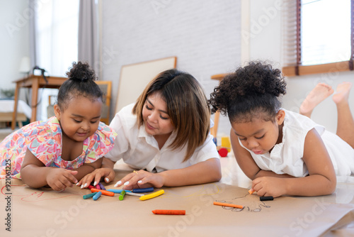 On a holiday, A woman and her two little daughters sit on the floor and drawing together in the living room