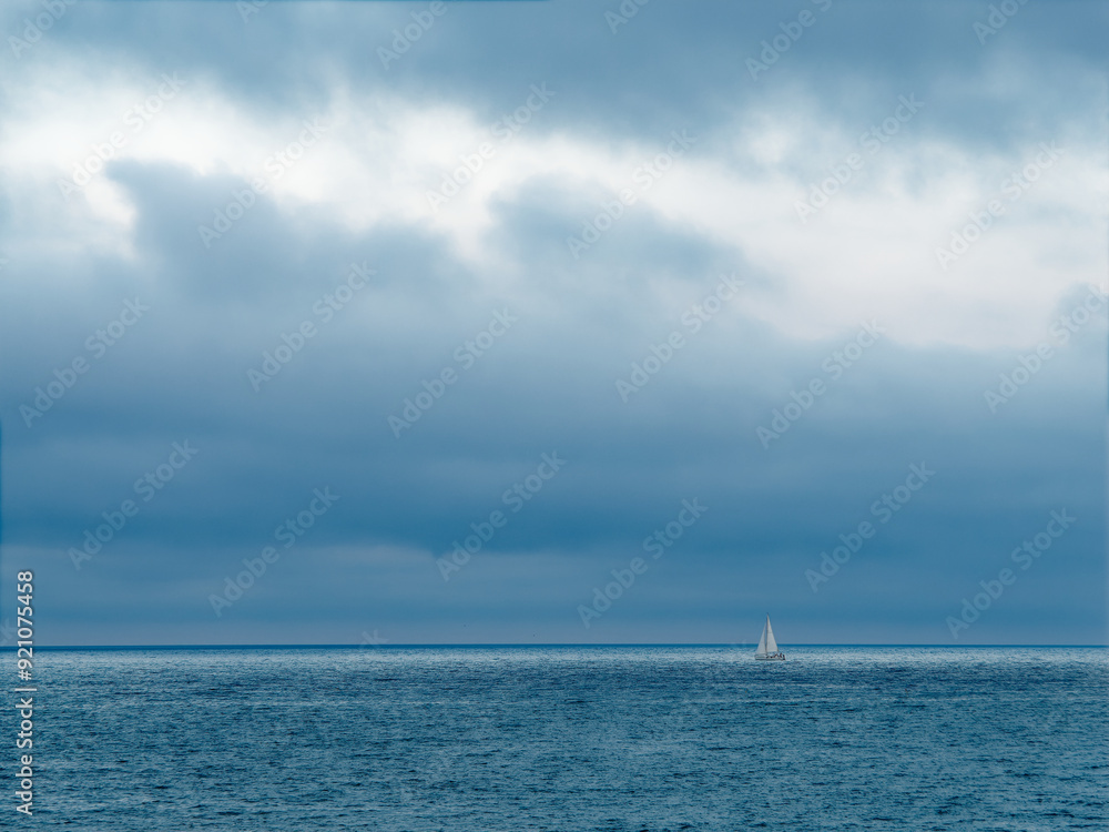 Calm sea with a distant sailboat under dark contrasted clouds, copy space, Palavas-les-Flots, France Calm sea with a distant sailboat under dark contrasted clouds, copy space, Palavas-les-Flots, France