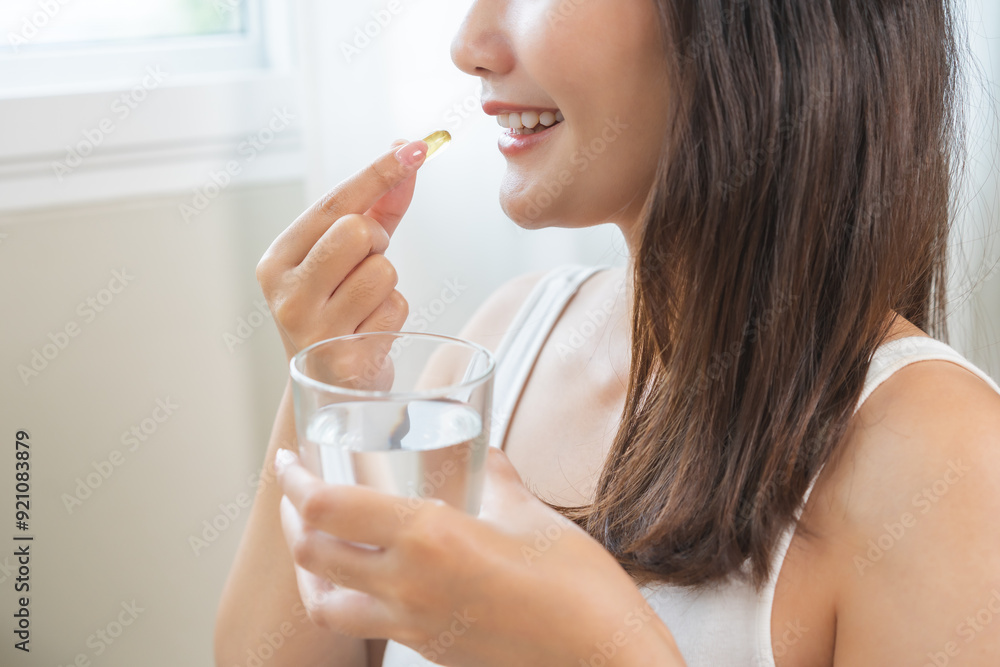 Dietary supplement, asian young woman, girl hand holding fish oil pills, drugs medical, take or eat vitamin for treatment skin, hair and nail strengthen with glass of water at home. Healthcare concept Dietary supplement, asian young woman, girl hand holding fish oil pills, drugs medical, take or eat vitamin for treatment skin, hair and nail strengthen with glass of water at home. Healthcare concept