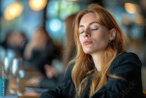 A businesswoman relaxes with closed eyes  momentarily escaping the lively meeting around her in a stylish cafe setting.
