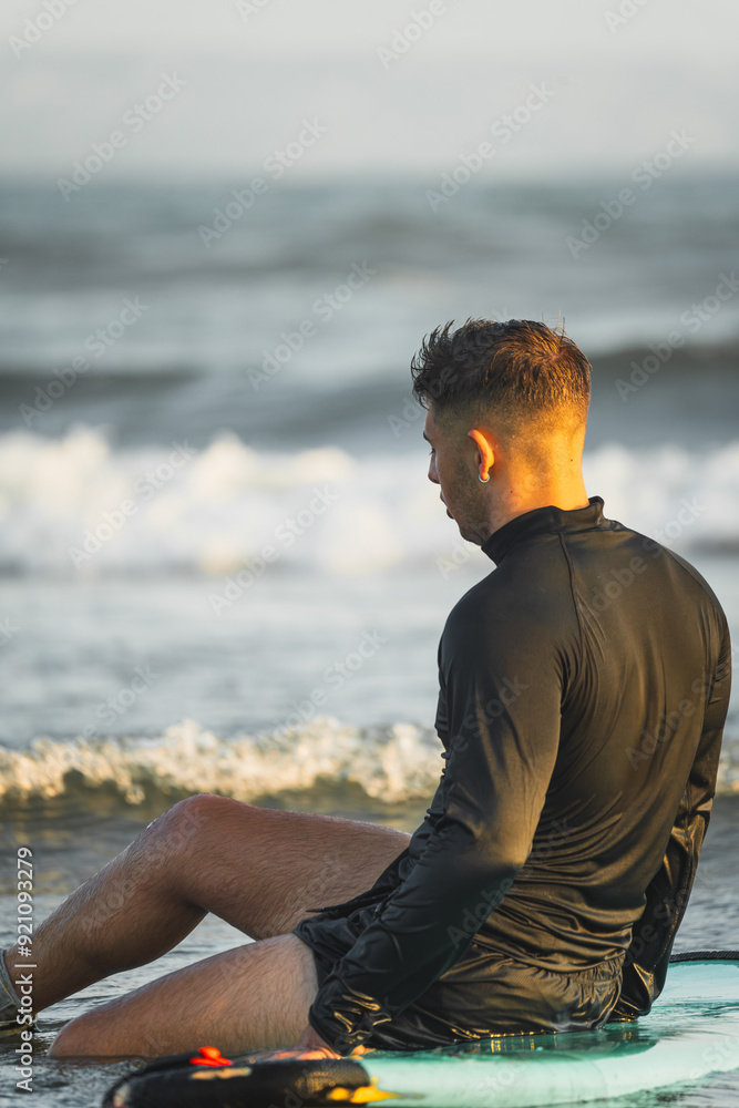 Surfer resting on his surfboard at the beach shore Surfer resting on his surfboard at the beach shore