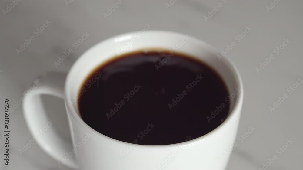 Close up on male hand adding sugar cube to a white cup of coffee Close up on male hand adding sugar cube to a white cup of coffee