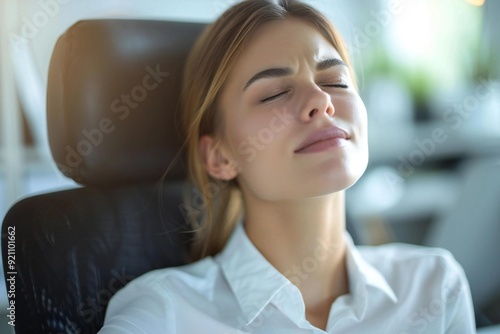 Close-up portrait of a young businesswoman sitting in an office chair, visibly in discomfort from back pain.