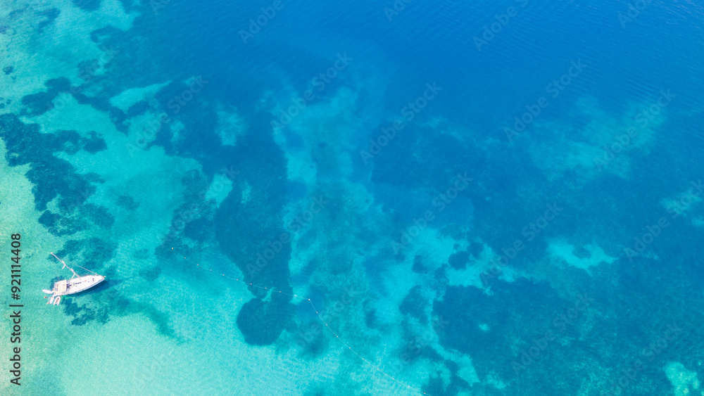 Fototapeta premium Aerial top-down view of a sailboat anchored in a turquoise bay on the beautiful Greece shore. Yacht on the water surface from top view. Summer seascape from air. Travel concept and idea