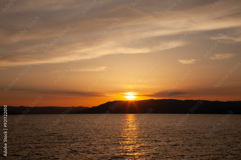 Sun going down on the horizon with red clouds over a mountain and lake Sun going down on the horizon with red clouds over a mountain and lake