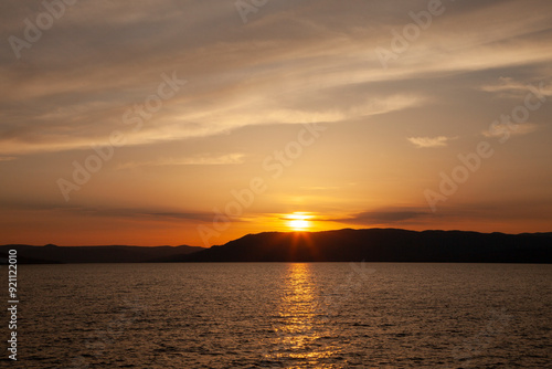 Sun going down on the horizon with red clouds over a mountain and lake