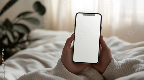 Person holding a smartphone with a blank screen. Cozy home environment with flowers, pillows and wicker decor, concept of relaxation and technology integration photo