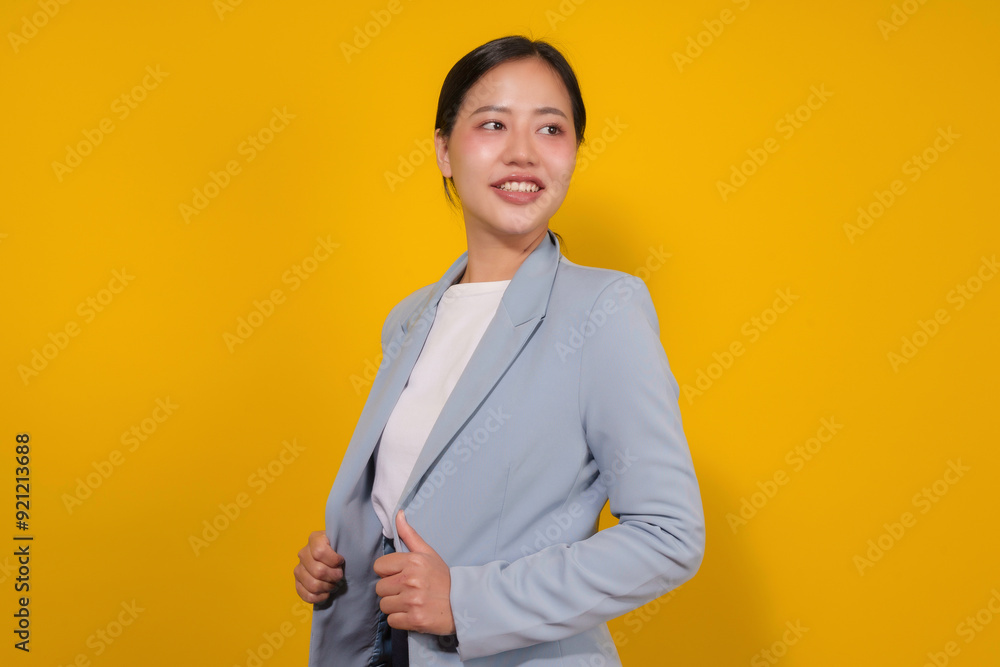 Young professional woman is smiling while adjusting her blazer against a vibrant yellow background Young professional woman is smiling while adjusting her blazer against a vibrant yellow background
