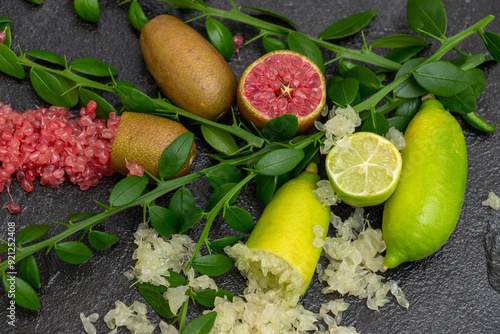 Ripe yellow and burgundy oblong citrus fruits with green sprigs on the black slate slab, close-up. Australian finger lime plant indoor growing. Microcitrus australasica, Faustrimedin photo